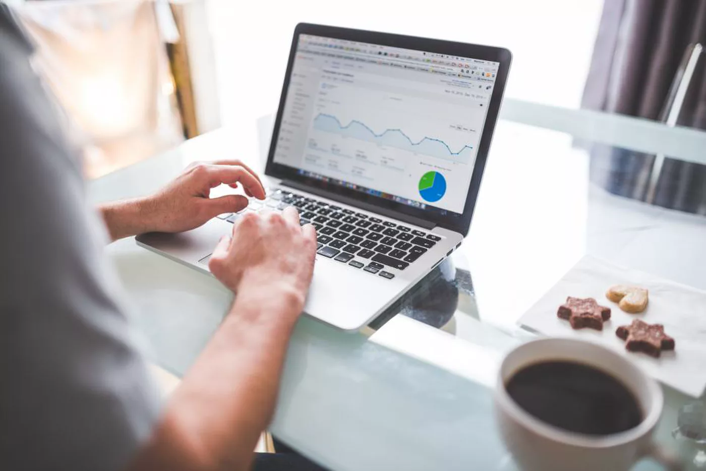 A person typing on a laptop that shows analytics charts, with a cup of coffee beside it
