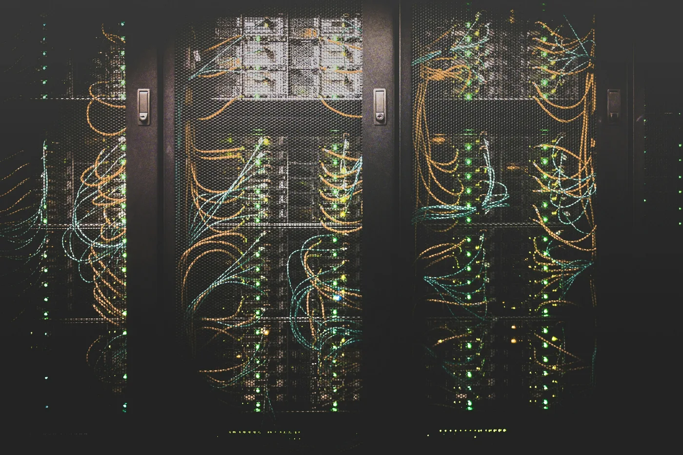 Server cabinets seen through mesh doors, filled with orange and blue patch cables and green status lights