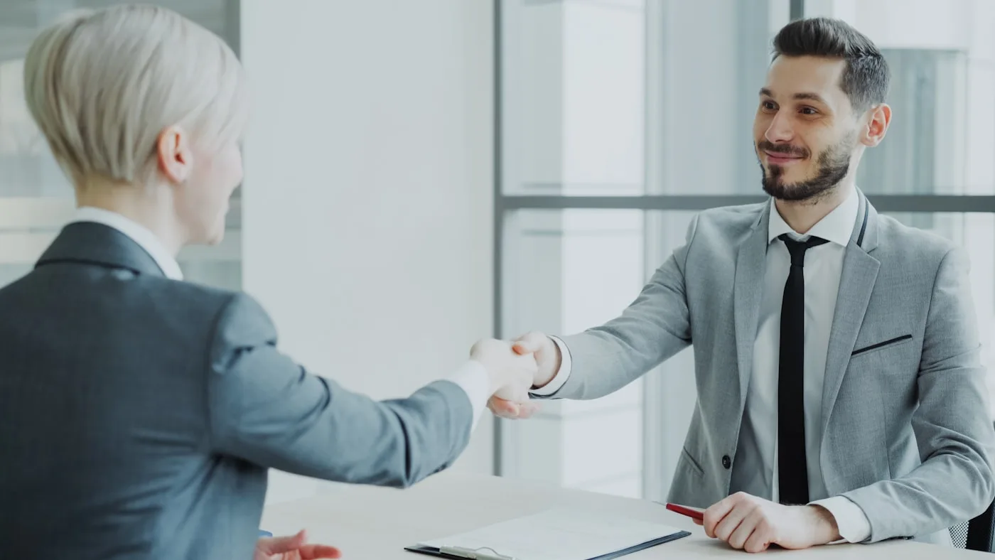 Two people shaking hands across a table in a modern office after a meeting