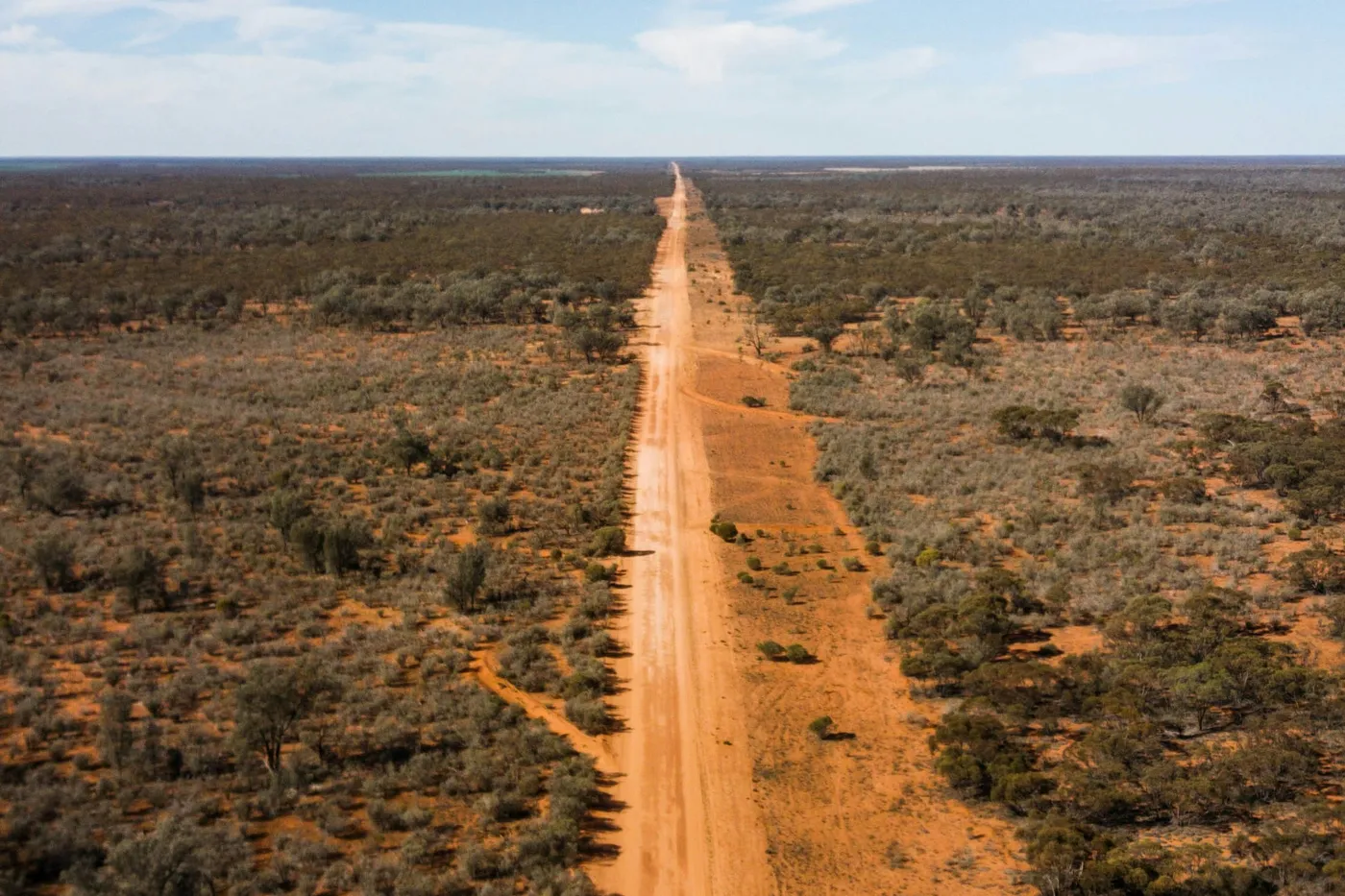 Aerial view of a red dirt road stretching to the horizon through the Australian outback with a lone truck